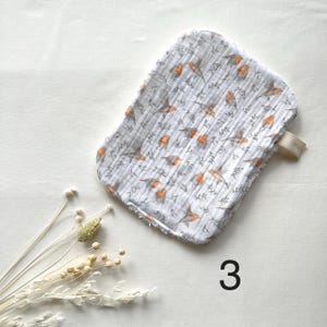 May include: A white and gray washcloth with a bird and leaf pattern. The washcloth has a loop and is decorated with orange birds and gray leaves. The number 3 is printed in black on the bottom right.