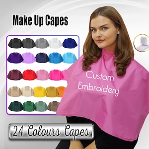 May include: A pink makeup cape with the text "Custom Embroidery" on the front. The cape is shown on a model with long brown hair. A selection of 24 different coloured capes is shown in the background. The text "Make Up Capes" and "24 Colours Capes" is also visible in the image.