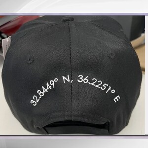 May include: Black baseball cap with white embroidered coordinates: 32.8449&deg; N, 36.2251&deg; E.