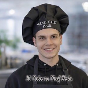 May include: A black chef hat with the text "HEAD CHEF PAUL" in white. The image also includes the text "30 Colours Chef Hats". The hat is worn by a person wearing a black hoodie and apron.