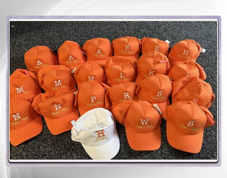 May include: A collection of 18 orange baseball caps with white embroidered letters and the text "Willy's Hats" on each cap. One white baseball cap with the letter "H" and the text "Get On It" is in the center of the image.