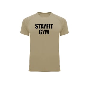 May include: A tan short-sleeved athletic shirt with the text "STAYFIT GYM" in bold black letters across the chest. The shirt has a crew neck and raglan sleeves. The background is plain white.