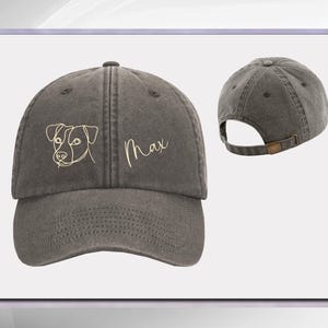 May include: A dark gray, adjustable, cotton baseball cap with a line drawing of a dog and the name "Max" embroidered in gold thread.