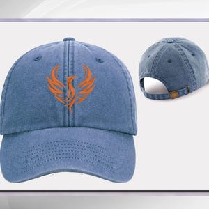 May include: A blue denim baseball cap with an orange phoenix design embroidered on the front. The cap has a curved brim and an adjustable strap.