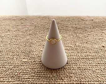 May include: A gold ring with a white stone set in a circle. The ring is displayed on a white cone-shaped ring holder.