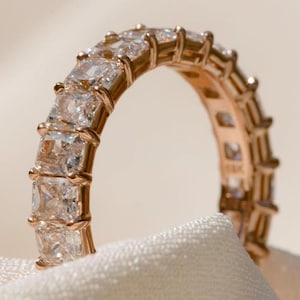 Op de afbeelding: Een gouden ring met een rij vierkante, heldere edelstenen.