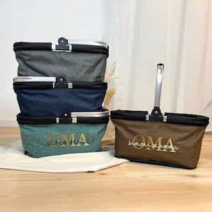 May include: Four foldable shopping baskets in grey, blue, and teal, with black trim and silver handles. One basket has the word "OMA" and a name embroidered on it.