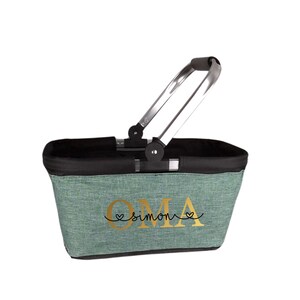 May include: A light green fabric basket with a black rim and a silver handle. The basket features the word "OMA" and the name "simon" in gold lettering with heart accents.