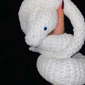 Op de afbeelding: Witte gehaakte slangen knuffel met blauwe ogen. De slang is opgerold in een spiraal.