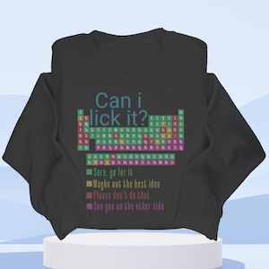 Peut inclure: Sweat-shirt noir avec l'inscription "Can i lick it ?" au-dessus d'un tableau périodique coloré. En dessous, quatre phrases : "Sure, go for it", "Maybe not the best idea", "Please don't do that" et "See you on the other side".