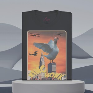 May include: A black t-shirt with a vintage-style graphic of a goose standing on top of a skyscraper in a city skyline. The goose is wearing a crown and the text "KING HONK" is below the goose. The graphic is set against a sunset background with airplanes flying overhead.