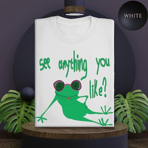 May include: White t-shirt featuring a green frog wearing pink sunglasses and the text "See anything you like?"