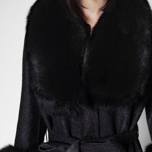 Pu&ograve; includere: Un cappotto grigio scuro con un ampio colletto e polsini in pelliccia nera. Il cappotto presenta una cintura abbinata annodata in vita. Il colletto e i polsini in pelliccia aggiungono un tocco lussuoso. Il cappotto &egrave; un capo di abbigliamento esterno elegante.