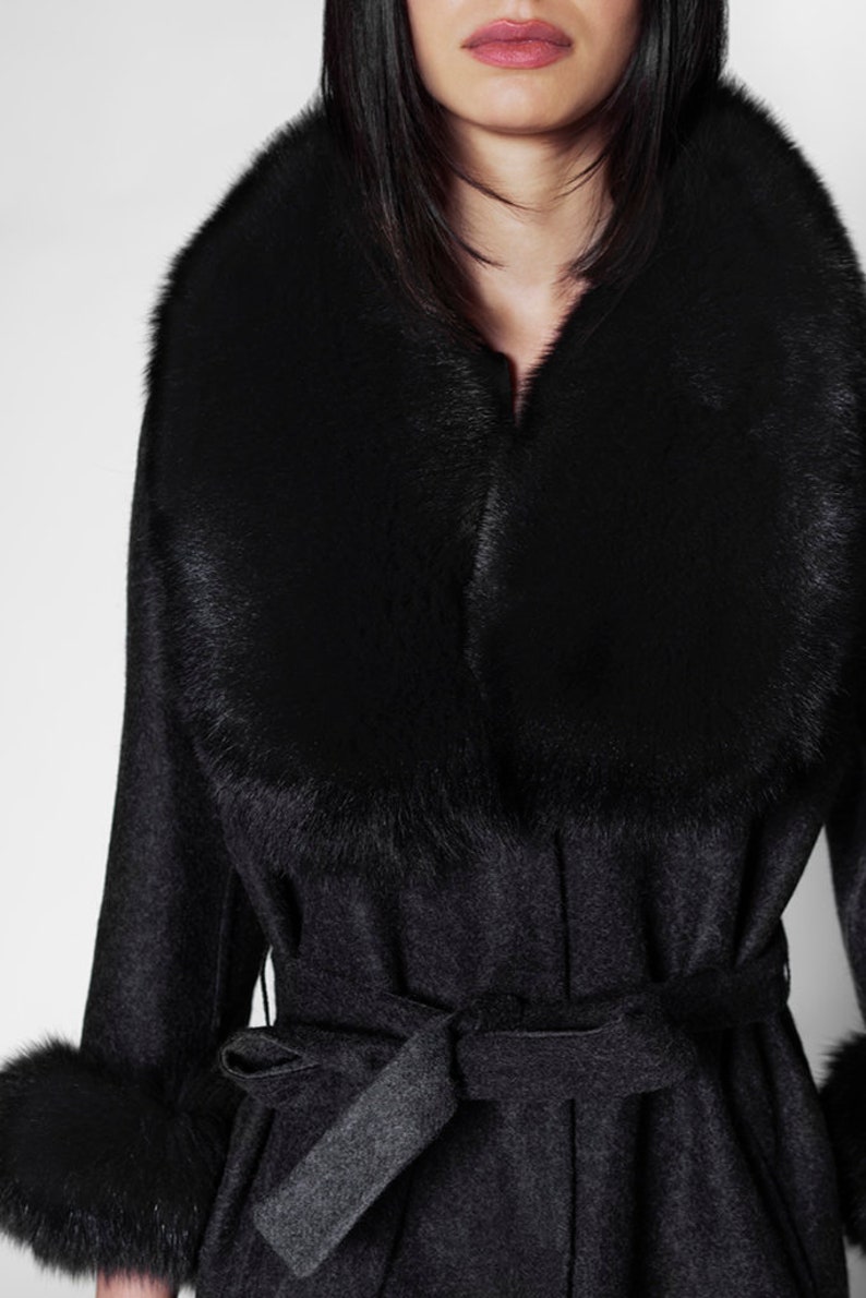 Pu&ograve; includere: Un cappotto grigio scuro con un ampio colletto e polsini in pelliccia nera. Il cappotto presenta una cintura abbinata annodata in vita. Il colletto e i polsini in pelliccia aggiungono un tocco lussuoso. Il cappotto &egrave; un capo di abbigliamento esterno elegante.