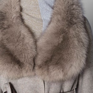 Pu&ograve; includere: Cappotto grigio chiaro con un ampio colletto in pelliccia soffice marrone chiaro. Il cappotto ha una cintura abbinata annodata a fiocco. Il colletto incornicia un dolcevita a due toni in argento e oro.