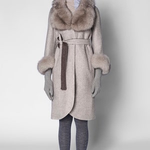 Pu&ograve; includere: Un cappotto beige chiaro con collo e polsini in pelliccia, cintura abbinata e cappuccio. Il cappotto &egrave; abbinato a guanti e collant grigi. Un capospalla elegante per il clima freddo.