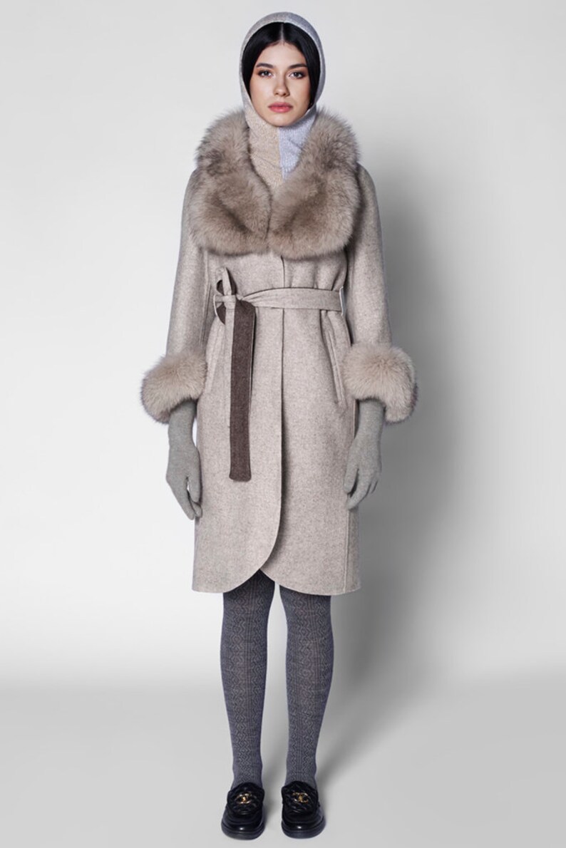 Pu&ograve; includere: Un cappotto beige chiaro con collo e polsini in pelliccia, cintura abbinata e cappuccio. Il cappotto &egrave; abbinato a guanti e collant grigi. Un capospalla elegante per il clima freddo.