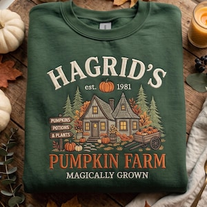 May include: A dark green crewneck sweatshirt featuring a graphic print of a house with the text "HAGRID'S est. 1981 PUMPKIN FARM MAGICALLY GROWN" and a sign pointing to "PUMPKINS POTIONS & PLANTS" surrounded by pine trees and pumpkins.