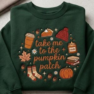 May include: A dark green crewneck sweatshirt featuring an embroidered design with the text "take me to the pumpkin patch" surrounded by icons of a coffee cup, pumpkin pie, beanie, candle, books, socks, acorns, and a maple leaf.