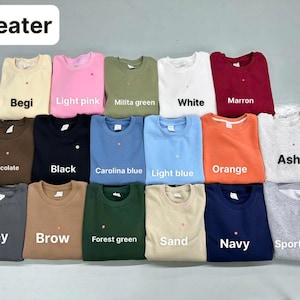 Pode incluir: Uma cole&ccedil;&atilde;o de dezasseis camisolas de gola redonda dispostas numa grelha, apresentando uma variedade de cores s&oacute;lidas, incluindo bege, rosa claro, verde militar, branco, castanho, chocolate, preto, azul Carolina, azul claro, laranja, cinza cinza, cinzento, castanho, verde floresta, areia, azul marinho e cinza desportivo.