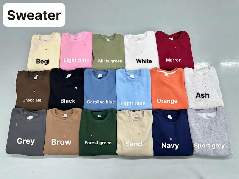 Pode incluir: Uma cole&ccedil;&atilde;o de dezasseis camisolas de gola redonda dispostas numa grelha, apresentando uma variedade de cores s&oacute;lidas, incluindo bege, rosa claro, verde militar, branco, castanho, chocolate, preto, azul Carolina, azul claro, laranja, cinza cinza, cinzento, castanho, verde floresta, areia, azul marinho e cinza desportivo.