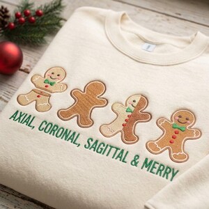 Peut inclure: Un sweat-shirt à col rond couleur crème orné de quatre personnages en pain d'épice brodés et du texte vert brodé "AXIAL, CORONAL, SAGITTAL & MERRY" situé sous les personnages sur le devant du vêtement.