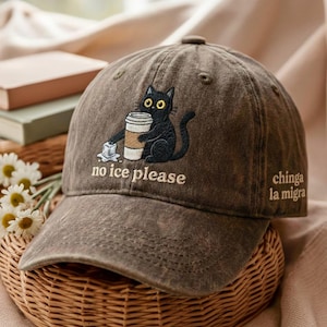 Puede incluir: Gorra de béisbol marrón con un diseño bordado de un gato negro sosteniendo una taza de café y cubitos de hielo. El texto "no ice please" está debajo del gato, y "chinga la migra" está en el lateral.