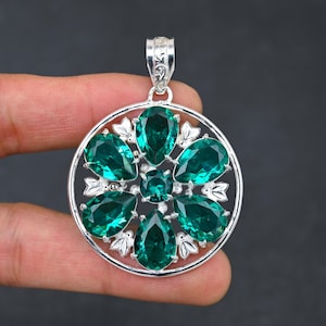 以下が含まれることがあります： 緑色の宝石の花がついた丸いデザインのシルバーペンダント。ペンダントは繊細なフィリグリーパターンで、どんな服装にもエレガントさを加えるのに最適です。
