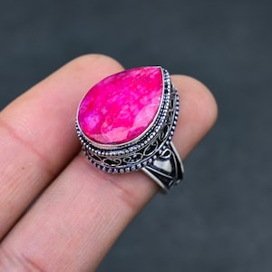 May include: A silver ring with an ornate design features a large, pear-shaped pink gemstone.
