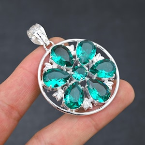 以下が含まれることがあります： 丸いデザインのシルバーペンダント。6つの緑色の宝石が花柄にセットされています。