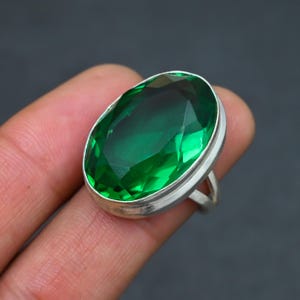 May include: A silver ring featuring a large, oval-shaped, green gemstone.