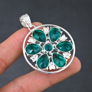 以下が含まれることがあります： 緑色の宝石の花がついた丸いデザインのシルバーペンダント。ペンダントにはチェーンに取り付けるためのベイルが付いています。