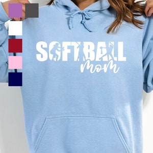 May include: A light blue hooded sweatshirt with the text "Softball Mom" in white. The text is surrounded by silhouettes of softball players.