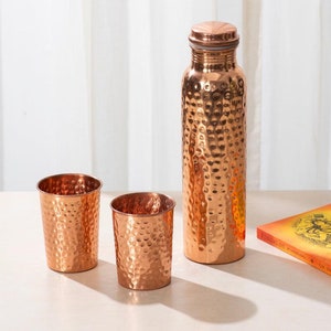 May include: A set of three copper drinking vessels with hammered texture. The set includes a tall bottle and two shorter cups.