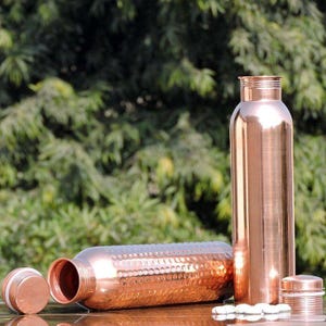 May include: Two copper water bottles, one with a hammered finish and the other with a smooth finish. Both bottles have lids.