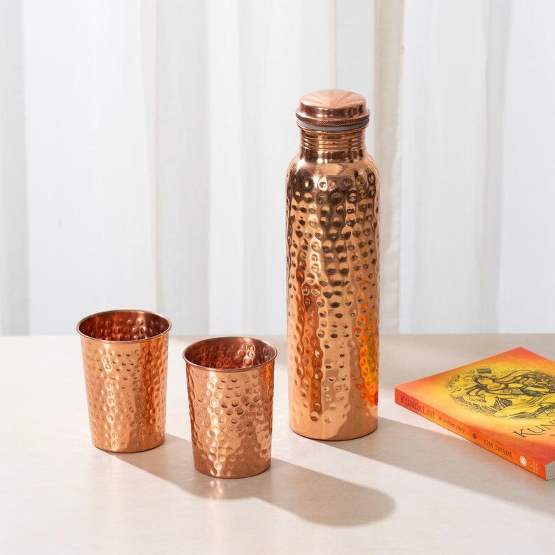 May include: A set of three copper drinking vessels with hammered texture. The set includes a tall bottle and two shorter cups.