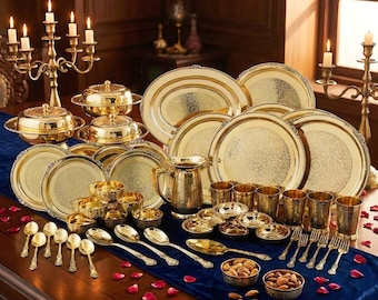 May include: A dining table is set with an opulent collection of gold-coloured tableware. The arrangement includes plates, serving dishes, bowls, spoons, forks, and glasses, all with intricate patterns. Candles in gold candelabras enhance the elegant atmosphere. The table is set for a feast.