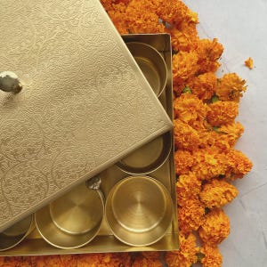Pode incluir: Uma caixa de metal dourado com um design ornamentado na tampa. A caixa est&aacute; aberta e tem seis compartimentos no interior. A caixa est&aacute; rodeada de flores de cal&ecirc;ndula laranja.
