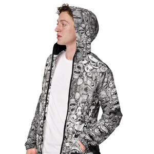 May include: A black and white zip-up hooded jacket featuring a repeating pattern of cartoonish monster faces. The jacket has a black zipper and a black interior lining. The person is wearing a white t-shirt underneath.