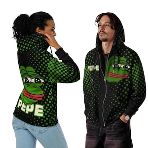 Könnte beinhalten: Schwarzer Kapuzenpullover mit Reißverschluss, mit einer grünen Froschgrafik und dem Wort "PEPE" in Weiß. Der Hoodie hat ein gepunktetes Muster in Grün und Schwarz. Die Froschgrafik befindet sich auf der Vorder- und Rückseite des Hoodies.