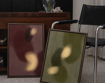 May include: Two framed abstract art prints. One is burgundy with a gold shape, the other is olive green with a gold shape. Both have dark brown frames. A vase of yellow flowers sits on a wooden cabinet.
