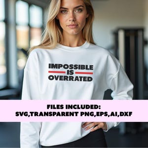 Peut inclure: Un sweat-shirt blanc avec le texte "IMPOSSIBLE IS OVERRATED" en lettres noires et rouges. Le texte est centré sur le sweat-shirt. Le sweat-shirt est porté par une personne dans un environnement de gymnase.
