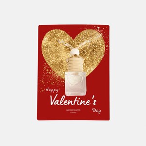 Puede incluir: Una tarjeta roja con un corazón de purpurina dorada y una pequeña botella de vidrio con una tapa de madera. El texto "Happy Valentine's Day" está escrito en cursiva blanca. La botella está etiquetada como "Aroma Moods Scented".