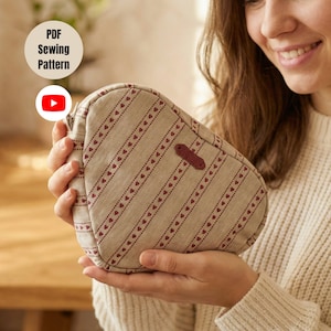 Könnte beinhalten: Eine beige, tropfenförmige Tasche mit einem sich wiederholenden Muster aus roten Herzen und Streifen. Die Tasche hat ein braunes Lederetikett und einen Reißverschluss. Die Worte "PDF Sewing Pattern" befinden sich in einem weißen Kreis oben links.