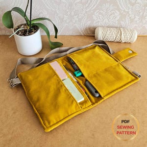 May include: Mustard yellow fabric organizer with multiple pockets, a gray shoulder strap, and a button closure. The organizer contains pens, a highlighter, and small notebooks. The text "PDF SEWING PATTERN" is in a circle on the bottom right.