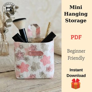 May include: A small, fabric hanging storage container with a white background and a pattern of pink and gray stars. The container holds makeup brushes and other items. The text "Mini Hanging Storage", "PDF", "Beginner Friendly", and "Instant Download" are visible.