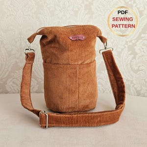 May include: A brown corduroy shoulder bag with a long adjustable strap and silver-tone hardware. The bag has a cylindrical shape with a zippered top and a small "handmade" label. The image also includes text that says "PDF Sewing Pattern".