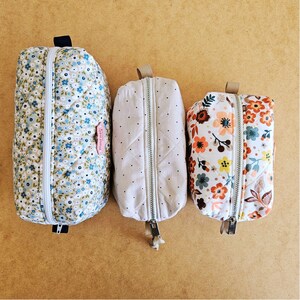 May include: Three quilted zippered pouches of different sizes. The largest has a blue floral pattern, the middle one a dotted design, and the smallest a floral print with orange, yellow, and blue flowers. Each pouch has a zip closure.