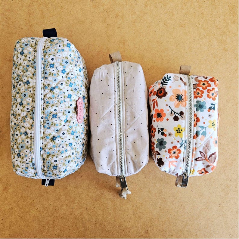 May include: Three quilted zippered pouches of different sizes. The largest has a blue floral pattern, the middle one a dotted design, and the smallest a floral print with orange, yellow, and blue flowers. Each pouch has a zip closure.