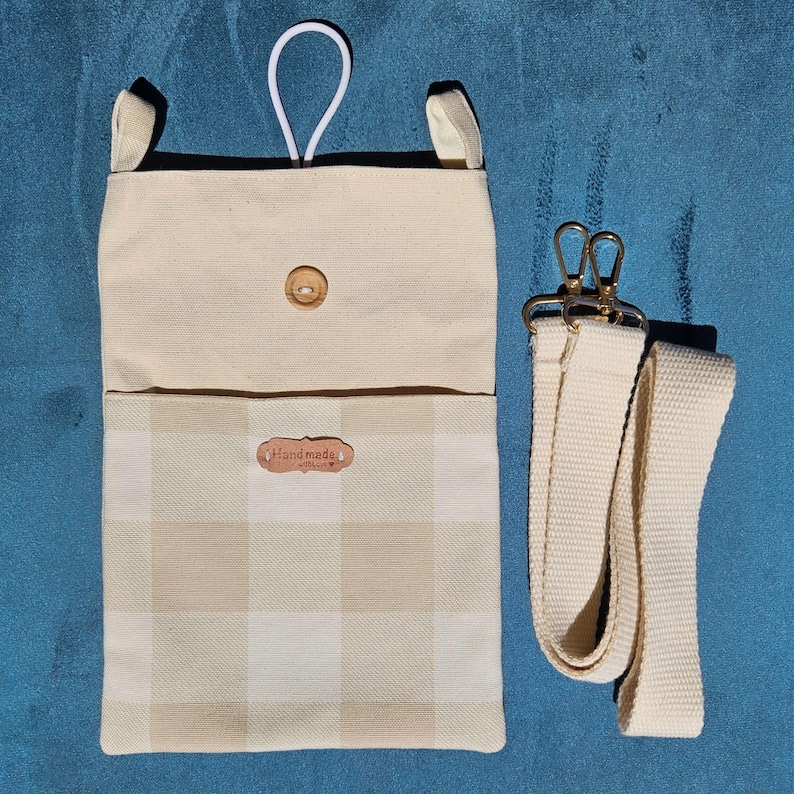 Op de afbeelding: Een handgemaakte stoffen tas in beige en cr&egrave;me met een ruitpatroon op de onderste helft. De tas heeft een houten knoopsluiting, een witte lus en een afneembare cr&egrave;mekleurige riem met goudkleurige sluitingen. Het label luidt "handmade with love".